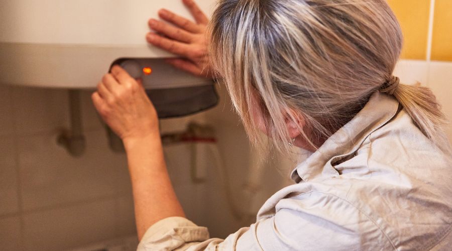 une femme observe de pres le voyant rouge fixe de son chauffe eau photo suggerant une anomalie ou panne dans le fonctionnement de l appareil 