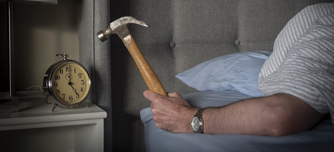 Personne fatiguée et énervée par le bruit de son réveil, tenant un marteau.