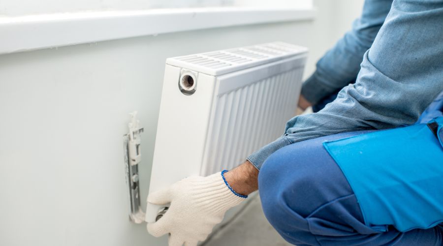 plombier chauffagiste fixant au mur un radiateur à eau chaude en aluminium pour illustrer le concept du prix de l'intervention