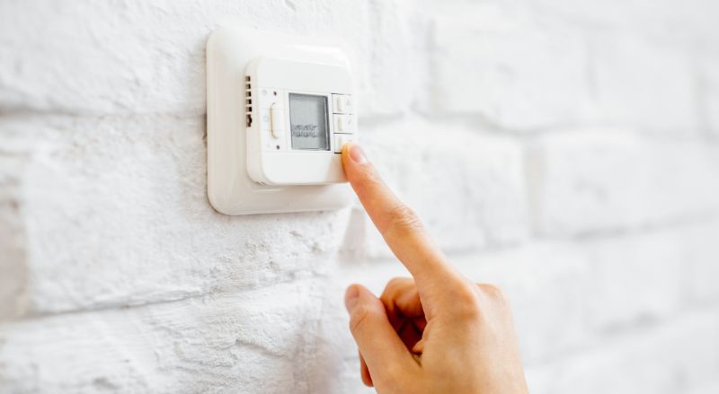 gros plan sur une main reglant un thermostat numerique pour plancher chauffant