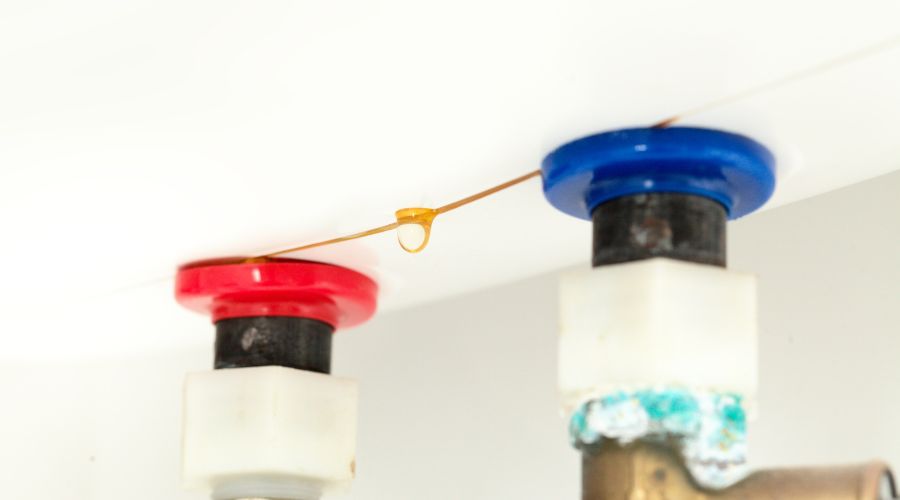 chaudière qui fuit avec une goutte d'eau visible formant une traînée depuis le raccord bleu