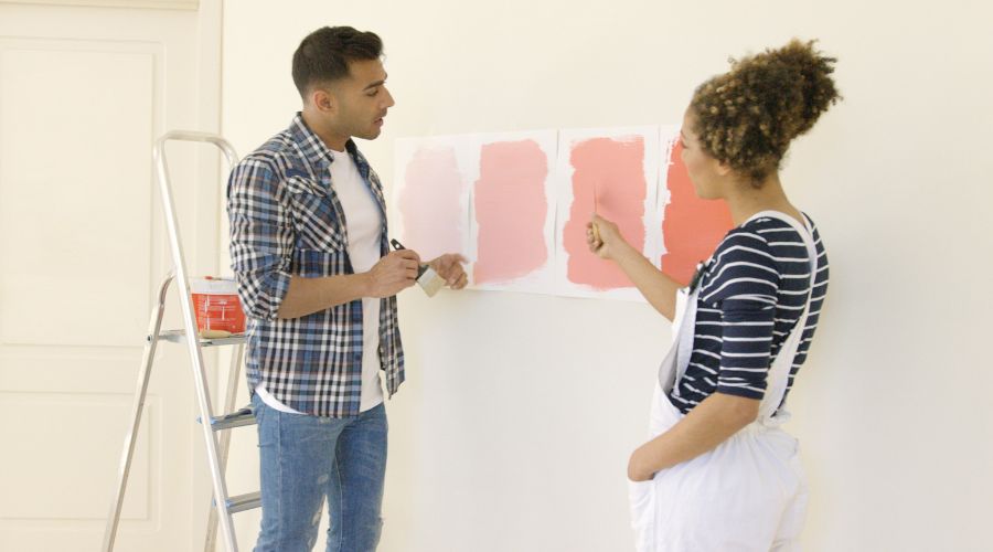 un jeune couple discute d une nouvelle couleur de peinture pour le mur de leur maison alors en affichant quatre feuilles format a4 sur le mur avec chacune une nuance de rose differente