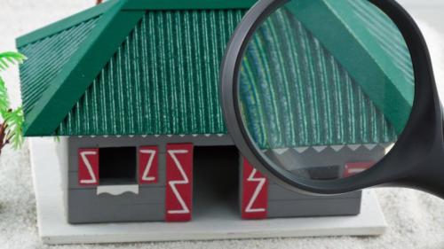maquette de maison avec une loupe devant la toiture, pour illustrer l'idée que, pour éloigner les souris de la maison, il faut aussi inspecter les points d'entrée par la toiture.