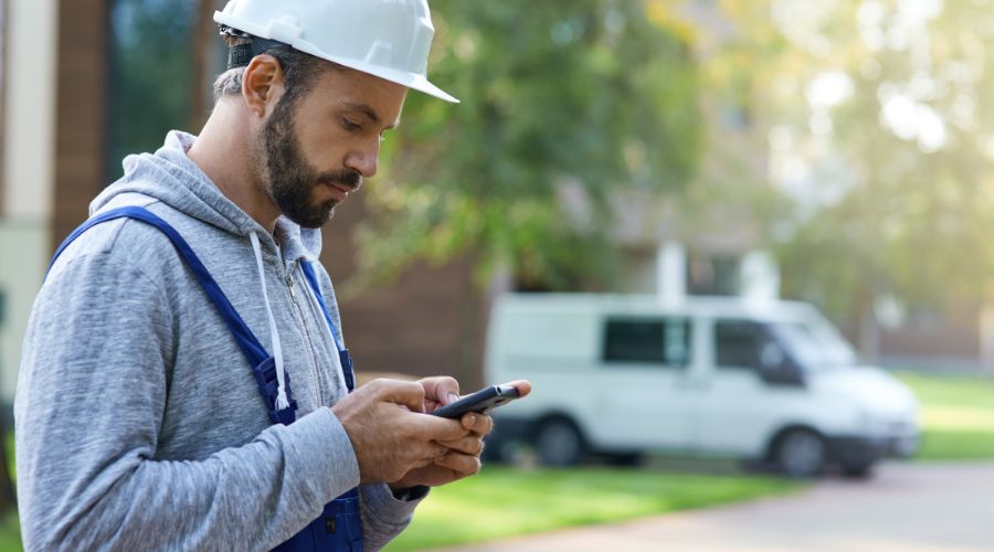 jeune pro debout à l'extérieur d'un chantier et tenant son smarphone pour illustrer le concept de relance téléphonique