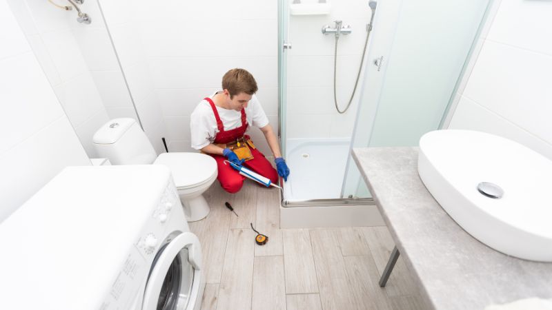 plombier avec un pistolet de silicone renovant le joint entre la cabine de douche et la paroi