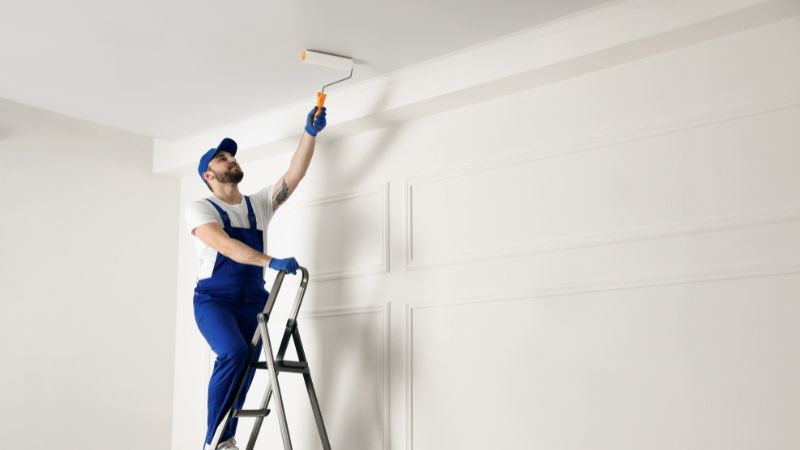 Peintre professionnel sur escabeau peignant un plafond au rouleau