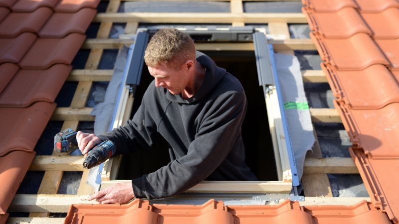 professionnel installant un velux sur un toit aux tuiles rouges