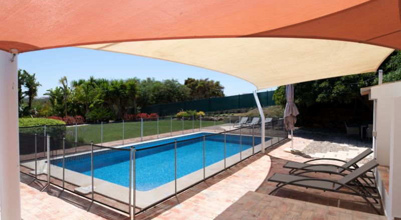 piscine cloturee dans un jardin avec transats sous voile d ombrage