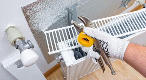 chauffagiste avec une cle et ruban de fil teflon posant une feuille disolation thermique sur le mur derriere le radiateur