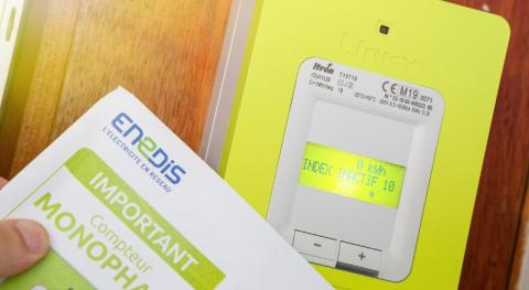 Tenue a la main un contrat d’ouverture enedis a cote d un compteur linky dans l entree d un batiment