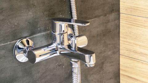 gros plan sur un mitigeur de douche fixé sur un carrelage gris