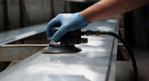 homme utilisant une ponceuse orbitale pour decaper de la peinture sur une surface en metal