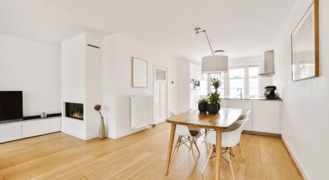 une piece de vie moderne et simple avec parquet flottant et murs blancs dont une table a manger en bois au centre de la piece